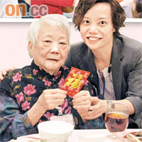 患有癡呆症的李婆婆接過利是後面露微笑，陪同婆婆出席活動的中心主任黃妙真（右）希望有更多敬老活動讓長者受惠。