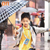 男童無懼黃色暴雨，蹦蹦跳打傘過馬路。