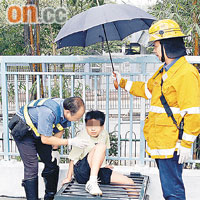 男童左腿被沙井蓋鐵枝夾實，消防員替他打傘設法拯救。