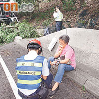 肇事巴士半邊車身騎上水渠蓋衝行，再撼大樹，一名傷者坐在路旁包紮。