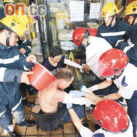救護員替傷者包紮傷口時，消防員淋水降溫。