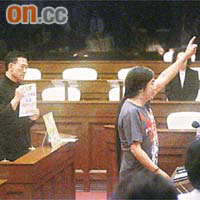 梁國雄舉手宣誓時，議員謝偉俊在其背後舉起「欠單」，指回歸立會議員欠全港市民一億五千萬元。